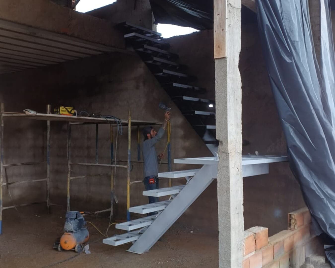 Escada metálica em fabricação e instalação dentro de obra, com profissional trabalhando na estrutura