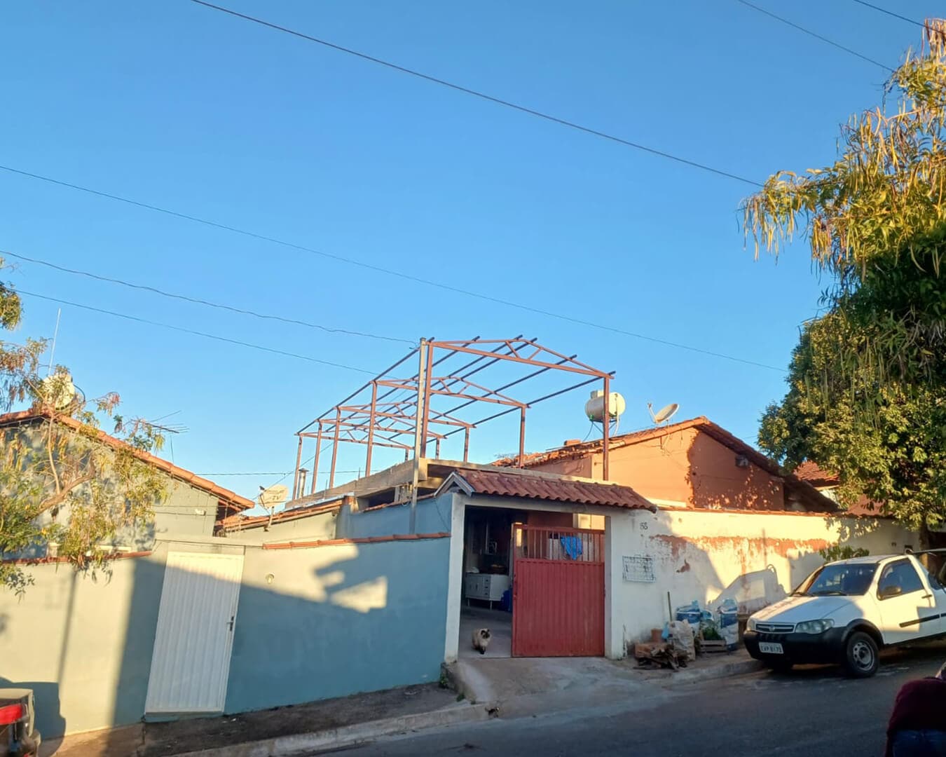 Estrutura metálica de sustentação de telhado sendo montada sobre casa, vista da rua