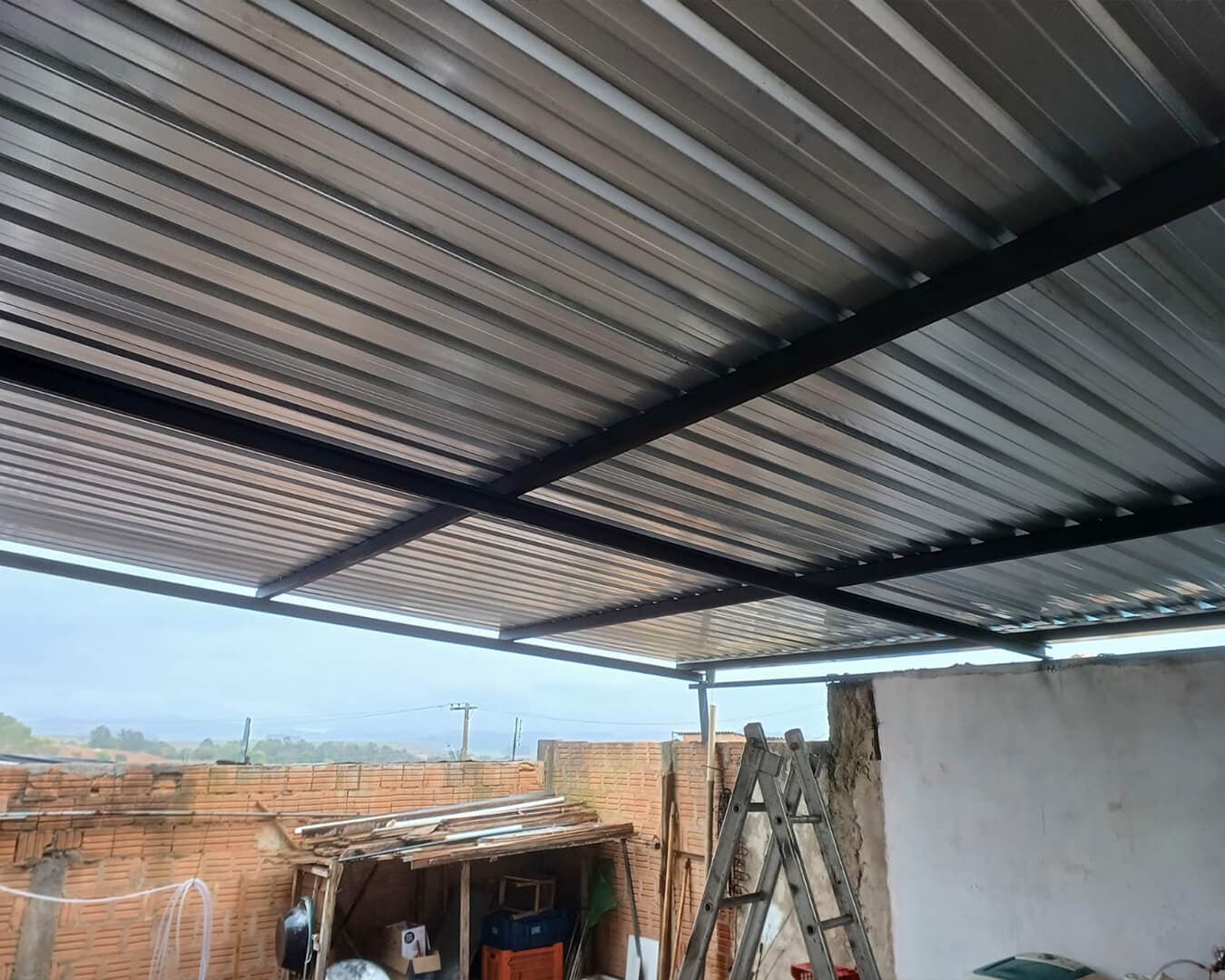 Cobertura metálica com telhas galvanizadas sobre estrutura de metalon, vista por baixo em quintal de casa