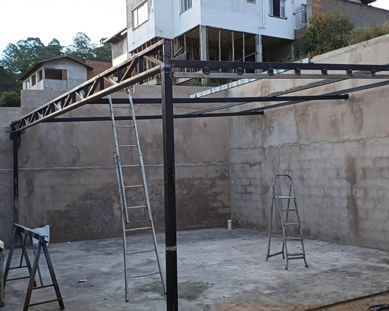 Estrutura metálica de cobertura em construção sobre paredes de alvenaria, com escadas e cavalete na obra